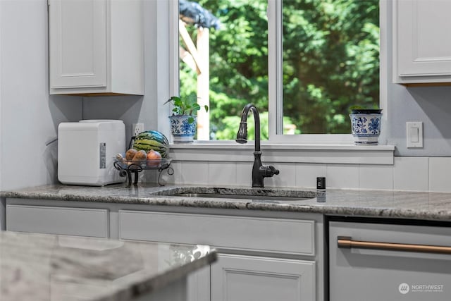 interior space featuring dishwasher, sink, white cabinets, and light stone countertops