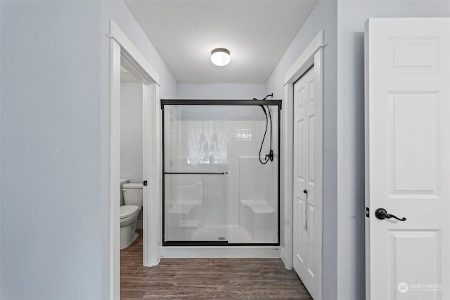 bathroom featuring toilet, a shower with door, and hardwood / wood-style flooring