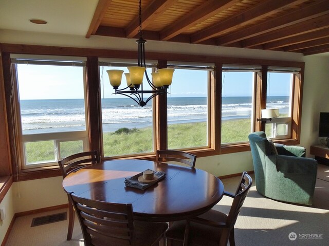 carpeted dining room featuring an inviting chandelier, beam ceiling, a healthy amount of sunlight, and a water view