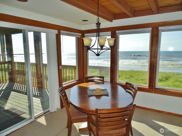 sunroom with wooden ceiling, an inviting chandelier, beamed ceiling, a water view, and a view of the beach