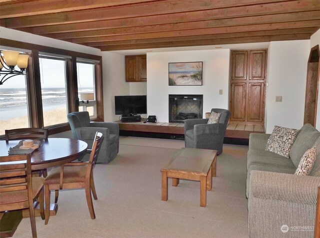 living room featuring an inviting chandelier, a water view, beamed ceiling, and light carpet