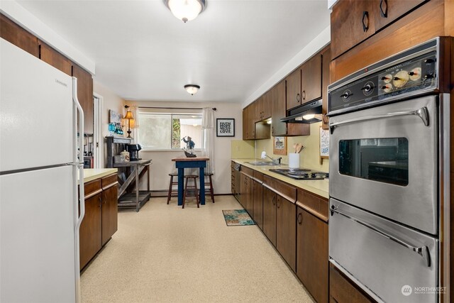 kitchen with double oven, gas stovetop, white refrigerator, dark brown cabinetry, and sink