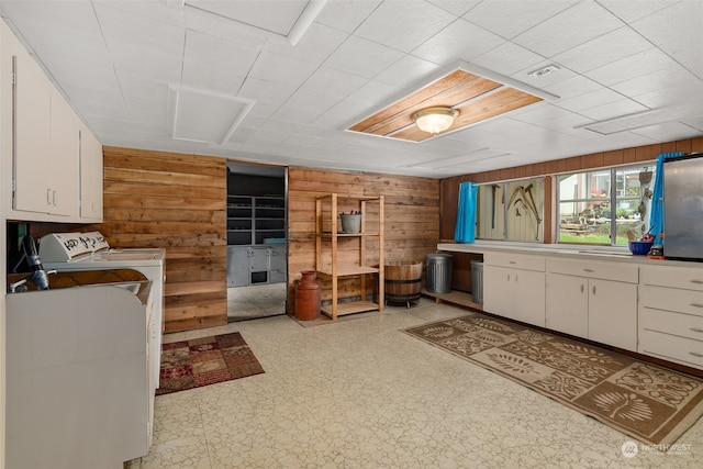 kitchen with white cabinets, wood walls, independent washer and dryer, and light tile floors