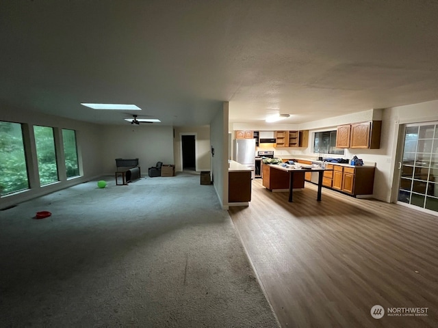 kitchen featuring a skylight, stove, a kitchen island, stainless steel refrigerator, and light colored carpet