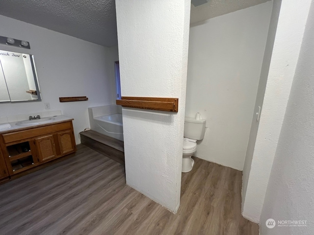 bathroom featuring oversized vanity, hardwood / wood-style flooring, toilet, a bath, and a textured ceiling