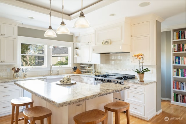 kitchen featuring a breakfast bar, backsplash, white cabinetry, and range with two ovens