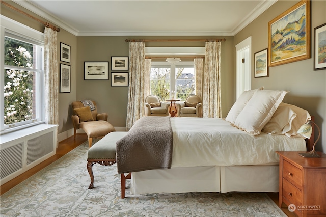 bedroom featuring radiator heating unit, crown molding, light wood-type flooring, and multiple windows