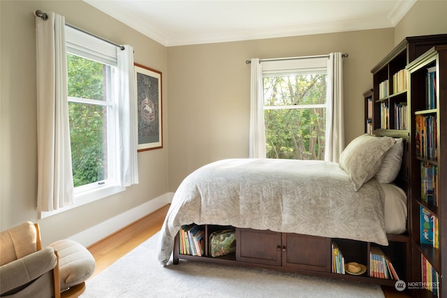 bedroom featuring multiple windows, crown molding, and light wood-type flooring