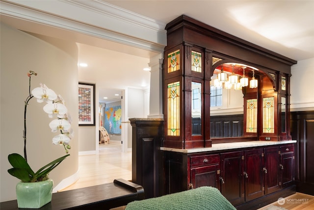 bar featuring ornamental molding, light stone counters, and light hardwood / wood-style floors