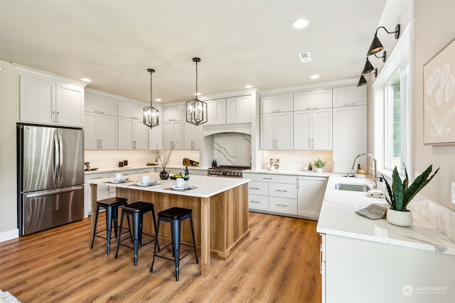 kitchen with white cabinets, sink, light hardwood / wood-style flooring, a kitchen island, and stainless steel appliances