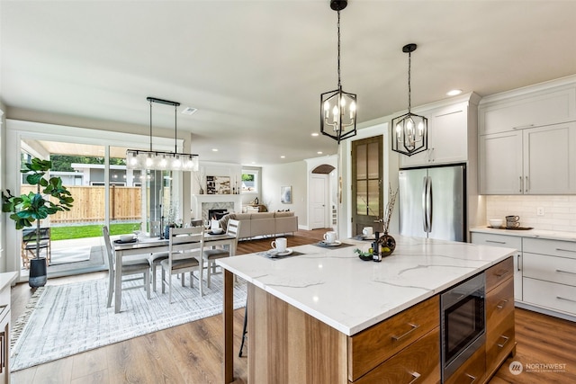 kitchen featuring stainless steel appliances, a kitchen island, decorative light fixtures, hardwood / wood-style floors, and white cabinetry