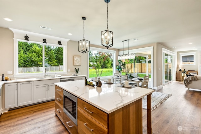 kitchen with sink, light hardwood / wood-style floors, a kitchen island, light stone counters, and stainless steel appliances