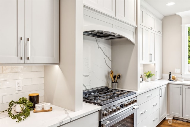 kitchen with stainless steel stove, light stone counters, backsplash, premium range hood, and white cabinets