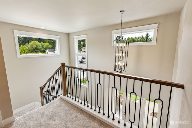 stairway featuring carpet floors, a wealth of natural light, and a chandelier