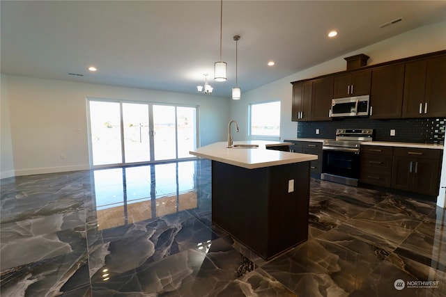 kitchen with backsplash, decorative light fixtures, stainless steel appliances, sink, and a kitchen island with sink