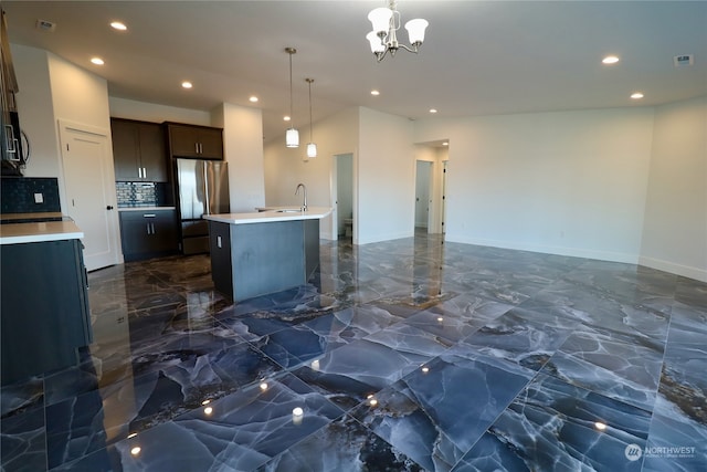 kitchen with decorative light fixtures, stainless steel fridge, a center island with sink, decorative backsplash, and dark brown cabinetry