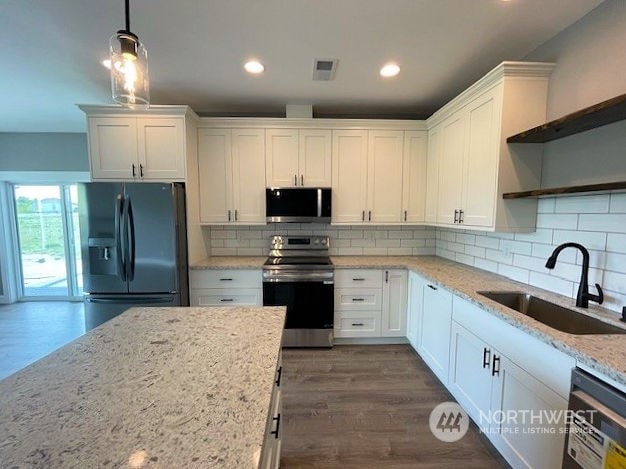 kitchen with appliances with stainless steel finishes, light stone countertops, pendant lighting, white cabinets, and sink