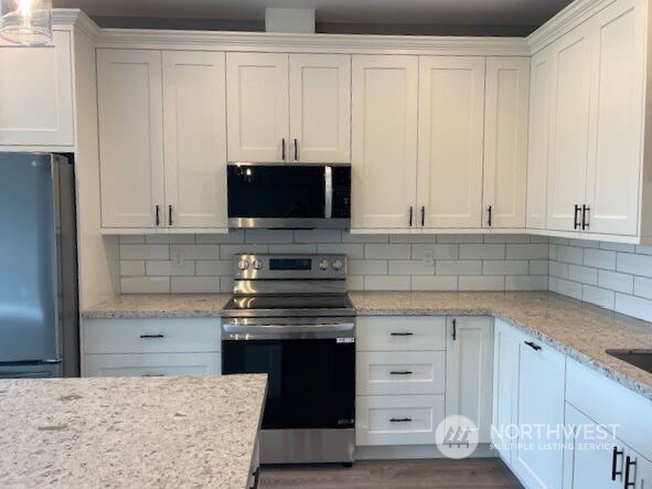 kitchen featuring stainless steel appliances, white cabinets, tasteful backsplash, light stone countertops, and dark wood-type flooring