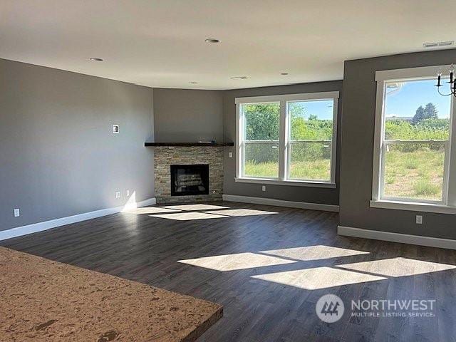 unfurnished living room with dark hardwood / wood-style flooring, a notable chandelier, a wealth of natural light, and a stone fireplace