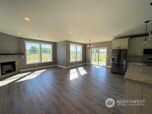 unfurnished living room featuring dark hardwood / wood-style flooring, a stone fireplace, and an inviting chandelier