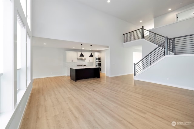 unfurnished living room featuring a towering ceiling, stairway, light wood-style flooring, and baseboards