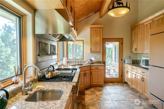 kitchen with beam ceiling, decorative light fixtures, a healthy amount of sunlight, and light stone countertops