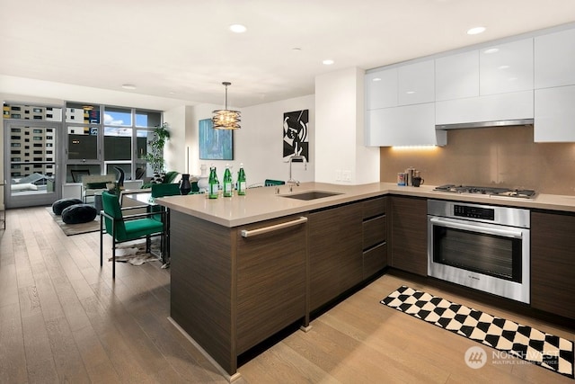 kitchen featuring kitchen peninsula, light hardwood / wood-style flooring, appliances with stainless steel finishes, white cabinetry, and sink