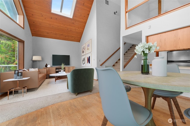 dining room featuring a skylight, light hardwood / wood-style floors, and high vaulted ceiling