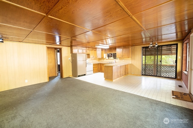 interior space featuring wooden ceiling, white appliances, light carpet, and wooden walls