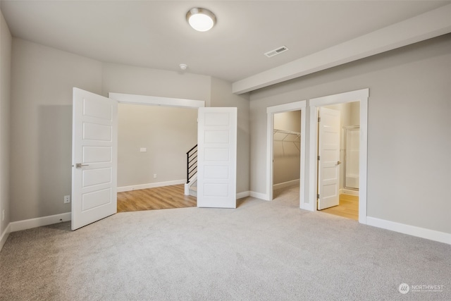 unfurnished bedroom featuring a closet, connected bathroom, a spacious closet, and light colored carpet