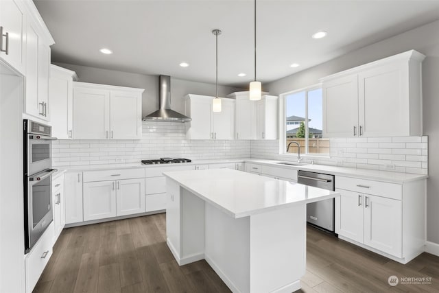 kitchen with tasteful backsplash, appliances with stainless steel finishes, wall chimney exhaust hood, and hardwood / wood-style flooring