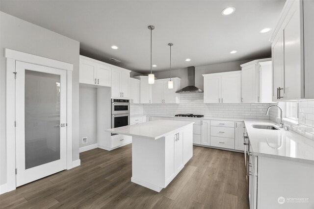 kitchen with appliances with stainless steel finishes, backsplash, hardwood / wood-style flooring, sink, and wall chimney range hood