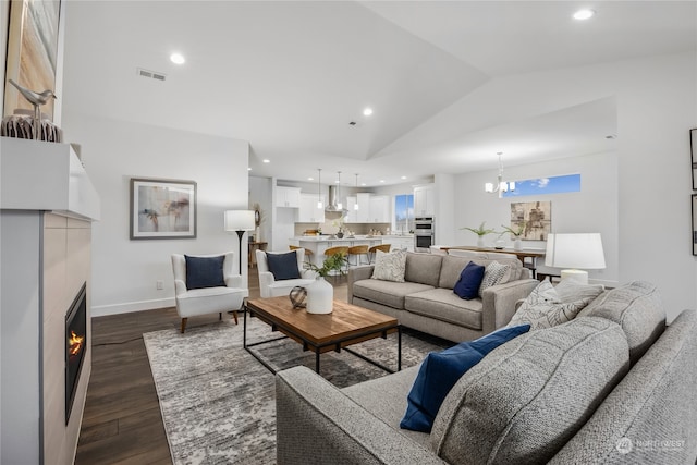 living room featuring dark wood-type flooring, vaulted ceiling, a tile fireplace, and a notable chandelier