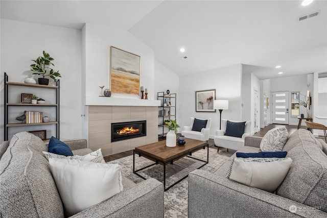 living room with a tiled fireplace, vaulted ceiling, and hardwood / wood-style floors