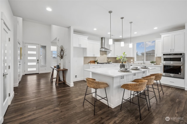 kitchen featuring pendant lighting, white cabinetry, a center island, and wall chimney exhaust hood