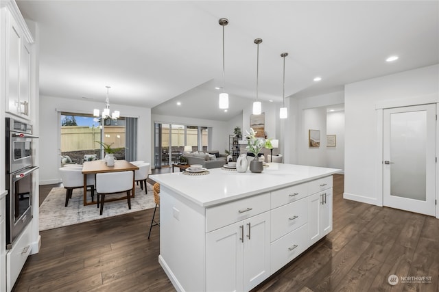 kitchen featuring white cabinetry, a breakfast bar area, dark hardwood / wood-style flooring, hanging light fixtures, and a center island