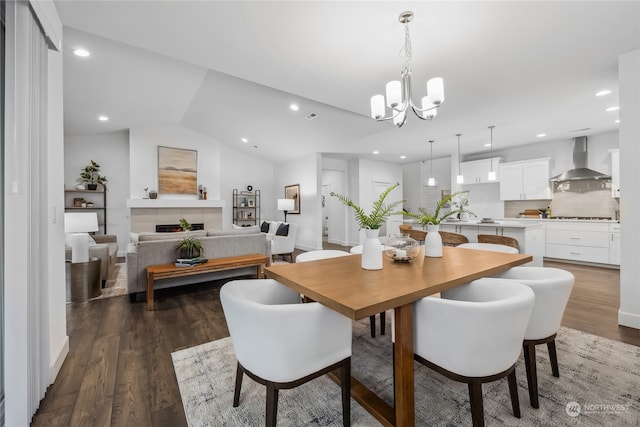 dining area with dark hardwood / wood-style flooring, vaulted ceiling, a fireplace, and an inviting chandelier