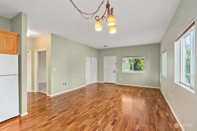 empty room with light hardwood / wood-style flooring, a wealth of natural light, and an inviting chandelier