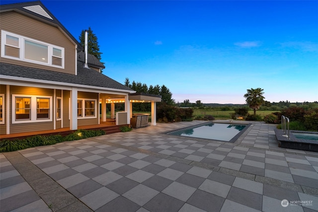 patio terrace at dusk featuring a pool with hot tub