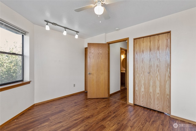 unfurnished bedroom with track lighting, a closet, ceiling fan, and dark hardwood / wood-style flooring