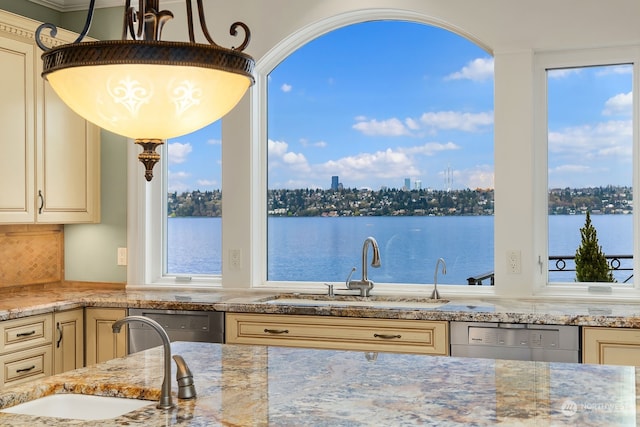 kitchen with stainless steel dishwasher, cream cabinets, sink, and light stone countertops