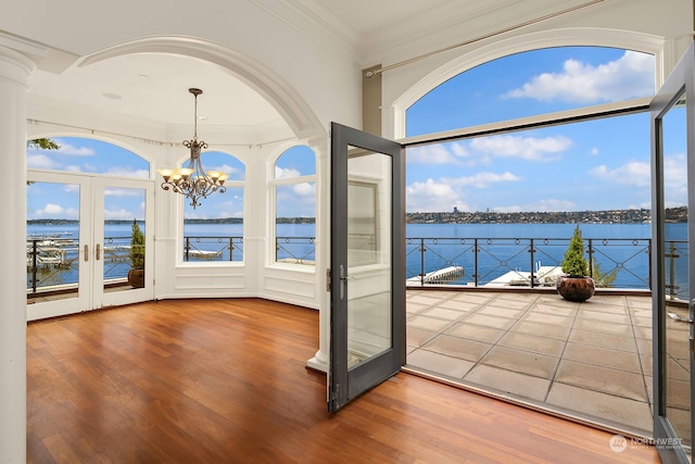 interior space with french doors, a notable chandelier, a water view, wood-type flooring, and ornamental molding