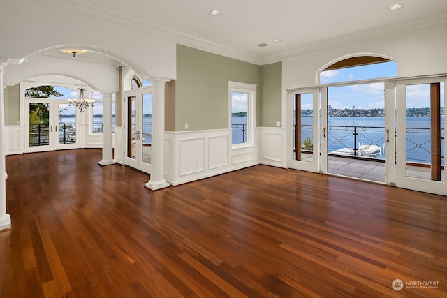 unfurnished living room featuring a water view, ornamental molding, dark hardwood / wood-style flooring, french doors, and ornate columns