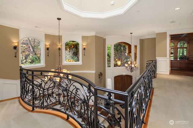 corridor with crown molding, an inviting chandelier, and light colored carpet