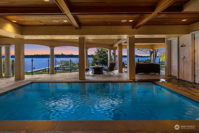 pool at dusk featuring a water view and a patio