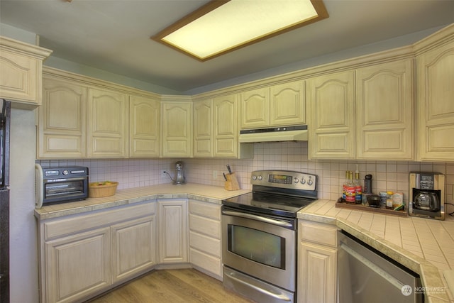 kitchen with light wood-type flooring, tasteful backsplash, tile counters, and appliances with stainless steel finishes