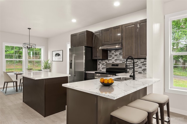 kitchen featuring light hardwood / wood-style floors, pendant lighting, kitchen peninsula, backsplash, and appliances with stainless steel finishes