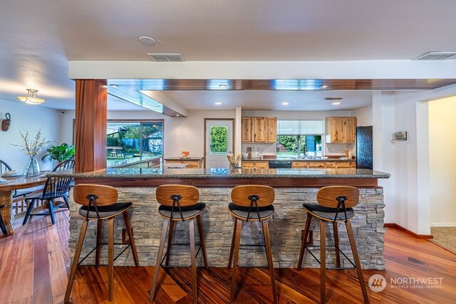 kitchen featuring dishwasher, dark stone countertops, dark hardwood / wood-style flooring, and a kitchen breakfast bar