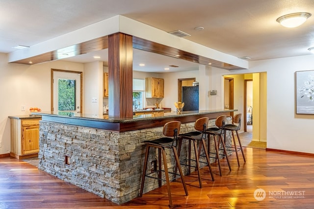 bar with black refrigerator, dark stone counters, and hardwood / wood-style flooring