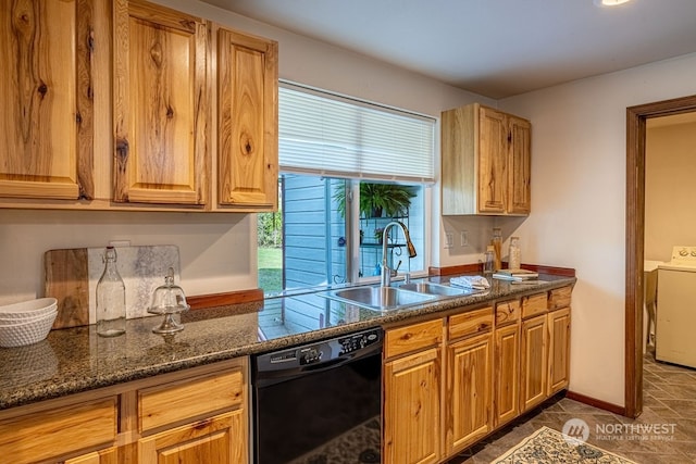 kitchen with dark stone countertops, dark tile flooring, dishwasher, sink, and washer / clothes dryer